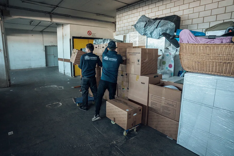 Zwei Mitarbeiter von Gerber Transport laden Umzugskartons auf einen Rollwagen